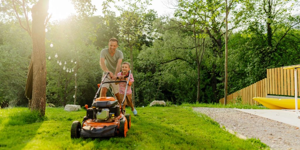 Photo of a young boy helping his father at mowing the lawn in their backyard