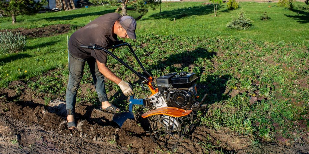 Male in the spring plows the earth in working clothes with a motoblock