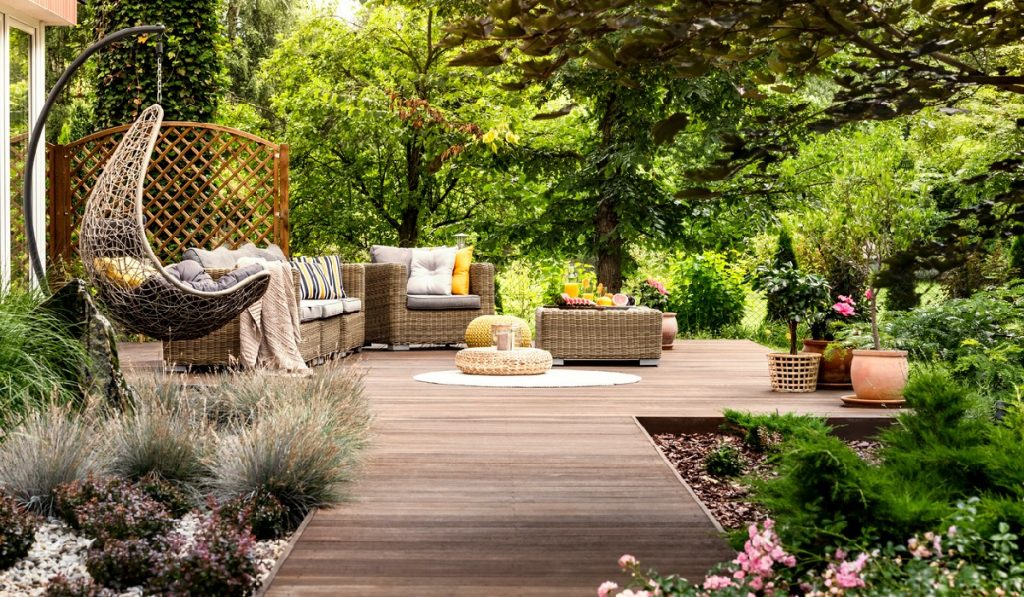 Beautiful wooden terrace with garden furniture surrounded by greenery on a warm, summer day