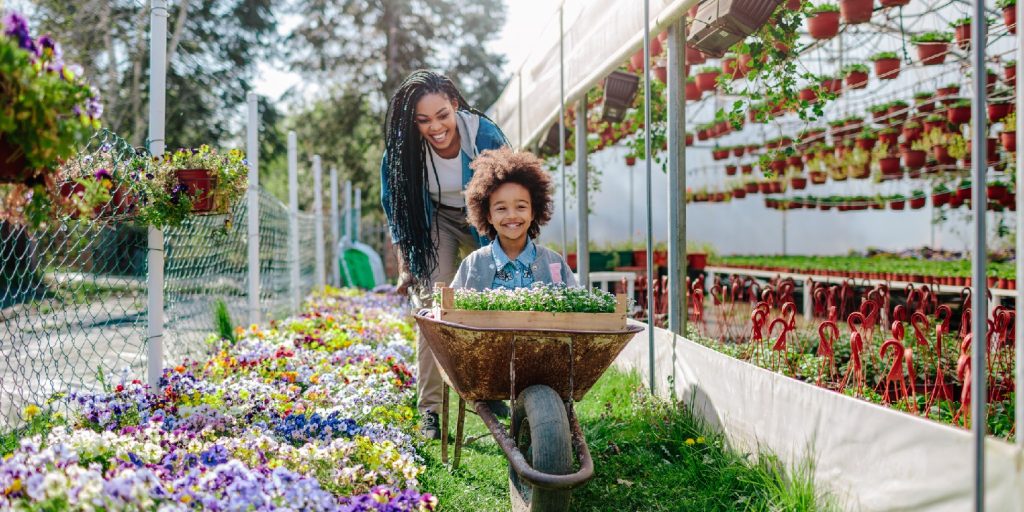 spring-gardening garden-gate Mother and daughter having fun, mother riding her cute daughter in wheelbarrow.