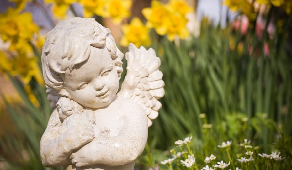 yard-art garden-gate Focus in on the angel. Tranquil scene, beautiful sunny day in the garden.