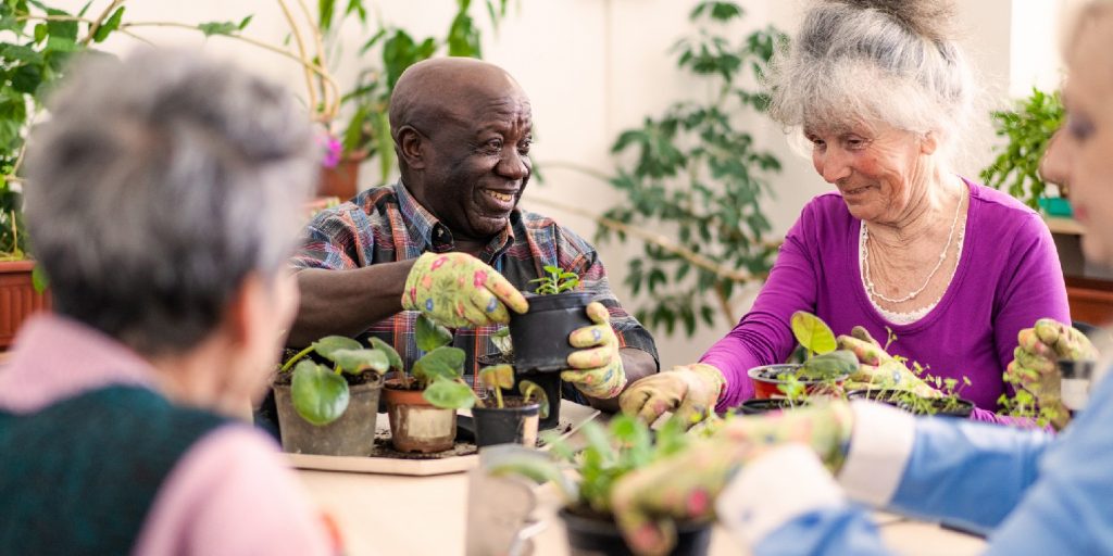 no-till-garden garden-gate Two smiling retired pensioners are tending to the potted plants on a table, in the foreground and out of focus more ladies are helping