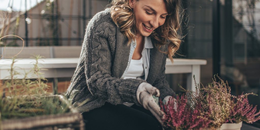 Photo of a young woman taking care of her rooftop garden on the balcony over the city, on a beautiful autumn day