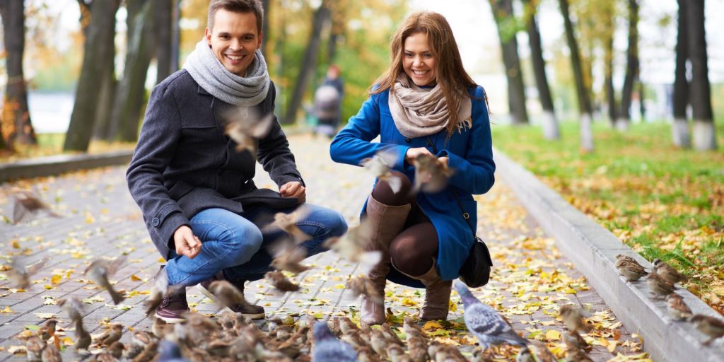 Fascinating young couple feeding birds in autumn park