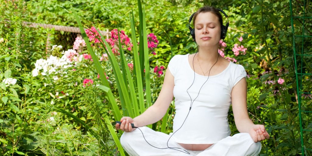 Pregnant Woman with Headphones Relaxing in a Garden