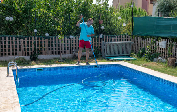 An image of a man cleaning his in-ground swimming pool with a pool vacuum hose